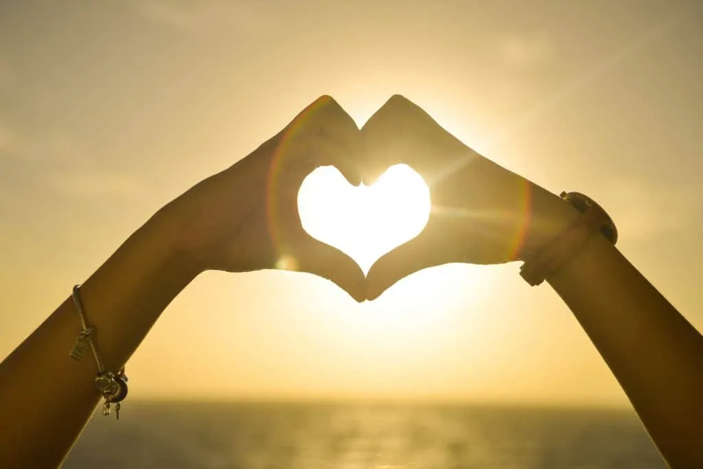 Hands forming a heart shape against a setting sun, symbolizing a loving tribute from Ashes to Space listing on US Funerals Online.