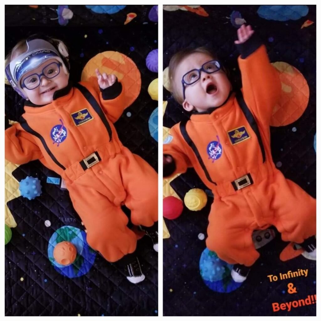 Ashtronaut Kindyn Rheed Jinkins' twin baby boys in NASA astronaut costumes on a solar system play mat, smiling and already reaching for the stars.