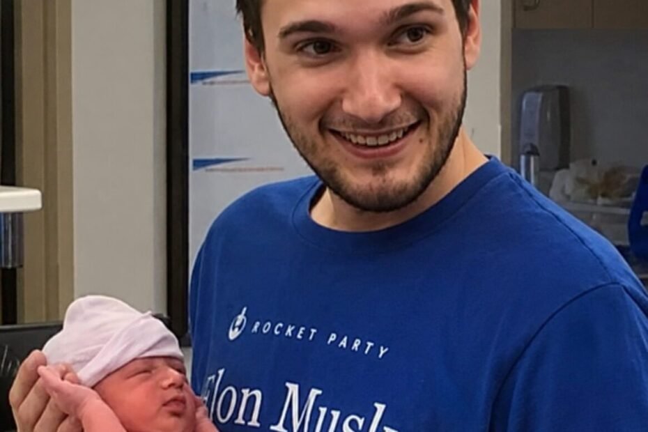 Kindyn Rheed Jinkins holding one of his newborn twin sons at the hospital, wearing a SpaceX-themed shirt — a proud father and dedicated space enthusiast, now an Ashtronaut on Space Beyond's Remembrance mission