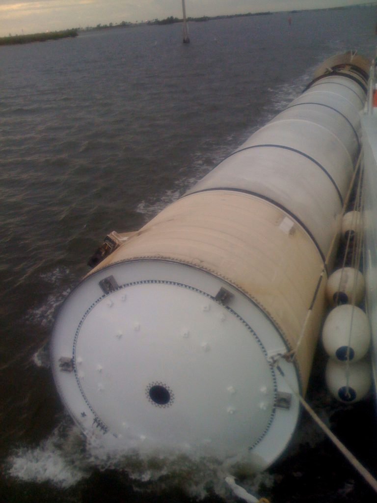 A recovered Space Shuttle Solid Rocket Booster being towed through calm water back to port.