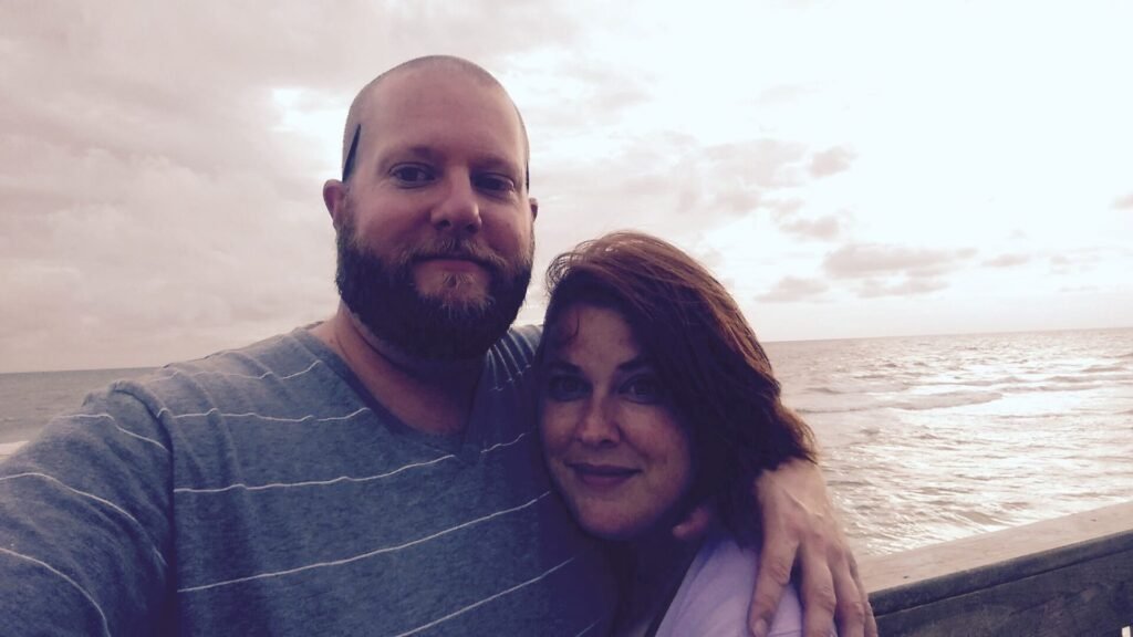 Ashtronaut Bryan J. Luther and his wife, Nicole, taking a selfie together on a beach at dusk.