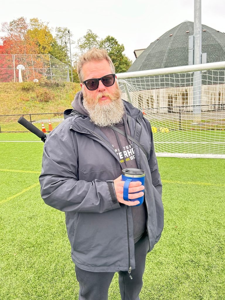 Ashtronaut Bryan J. Luther standing on a soccer field, wearing a Pittsburgh Riverhounds SC hoodie and holding an insulated tumbler.