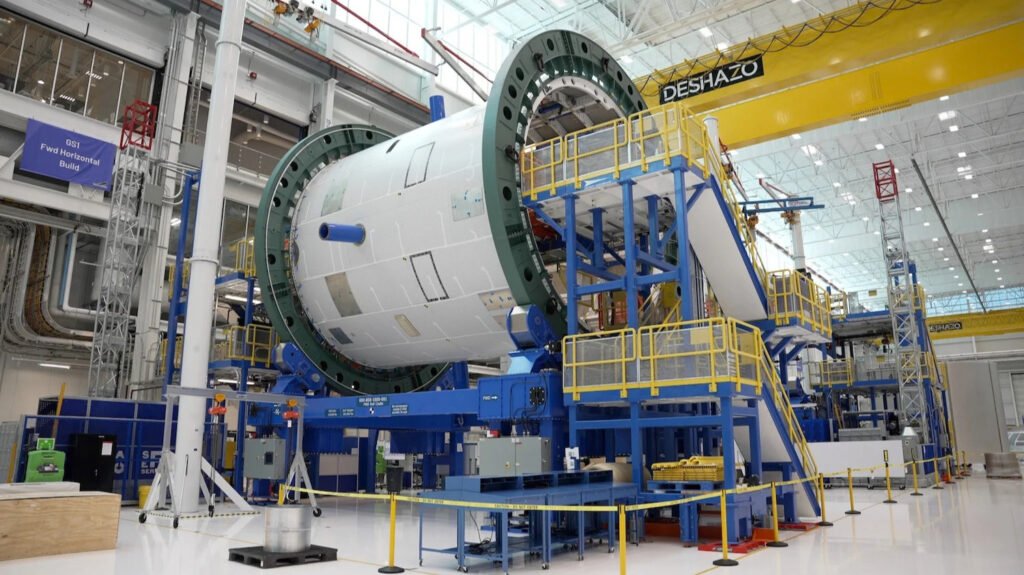 A New Glenn rocket forward section mounted in factory tooling at Blue Origin, surrounded by catwalks and an overhead crane.