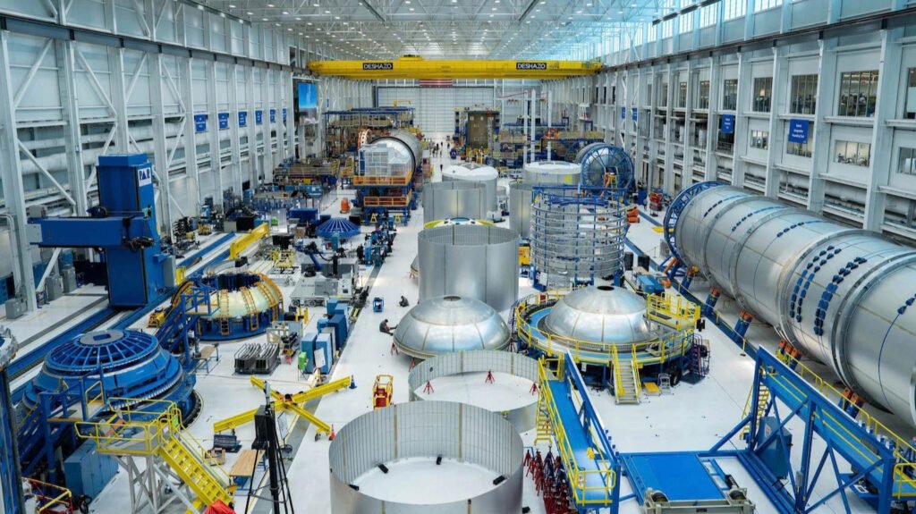 Interior of Blue Origin's New Glenn manufacturing facility, a high-bay factory floor with large rocket stage segments, tooling, and an overhead gantry crane.