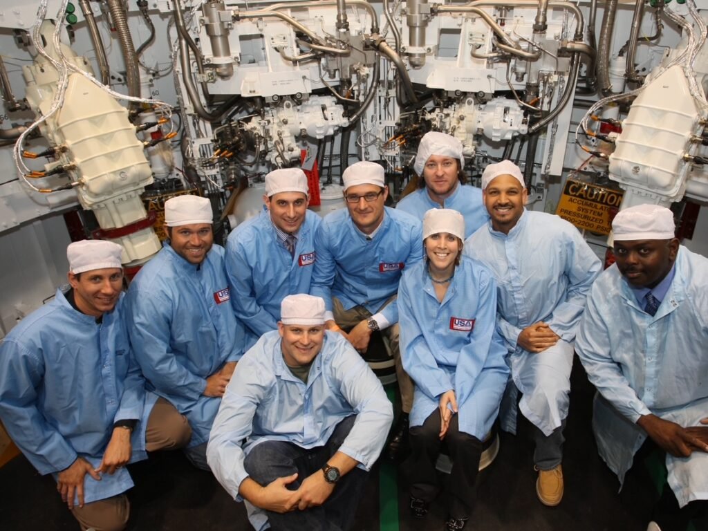Space Beyond founder Ryan Mitchell's United Space Alliance team posing together in white cleanroom coveralls, hoods, and masks inside a Space Shuttle Solid Rocket Booster segment during assembly.